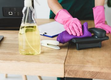 cropped shot of woman in rubber gloves cleaning telephone on table in office